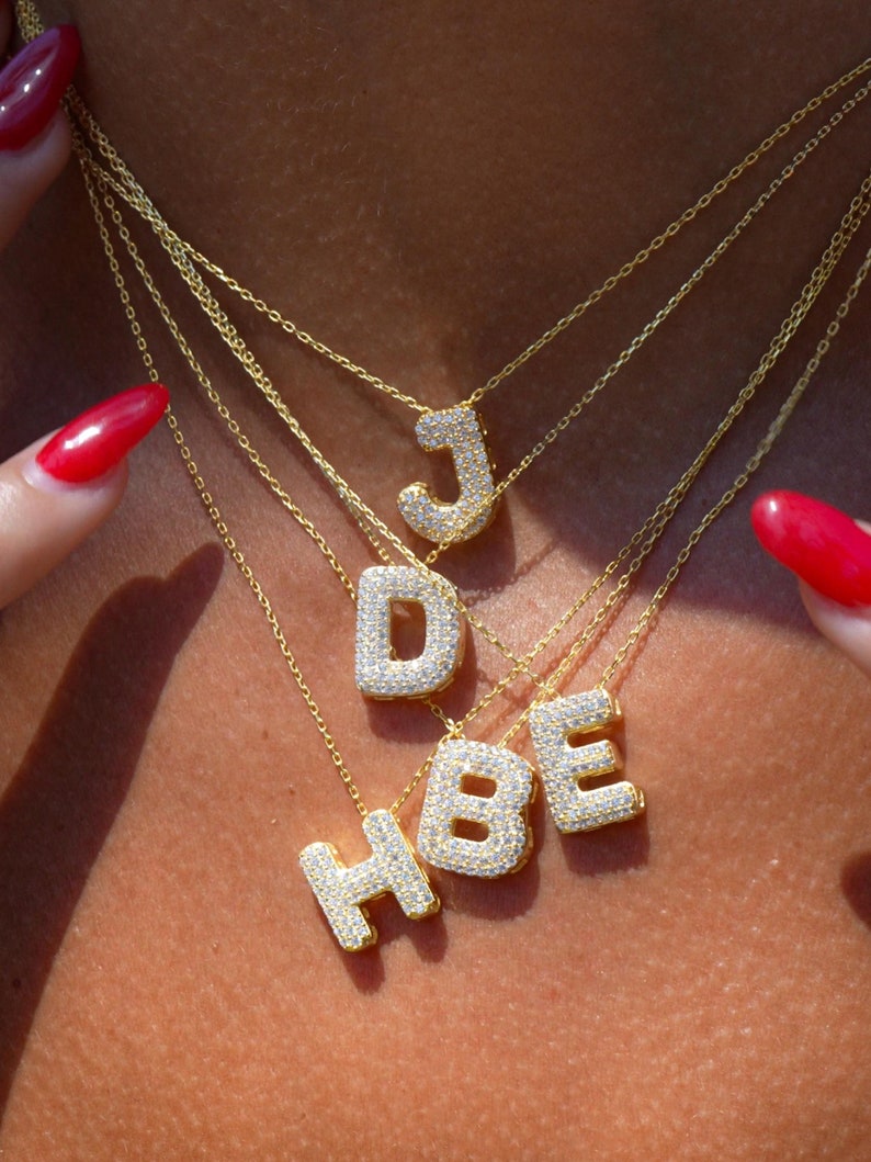 Puede incluir: Cuatro collares de oro con colgantes de letras engastados con diamantes. Las letras son J, D, B y H.