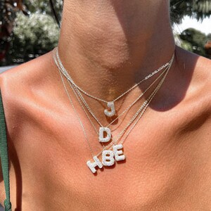 Puede incluir: Primer plano del pecho de una mujer que lleva un collar de capas con letras engastadas en diamantes que deletrean "HBE" y "JD".