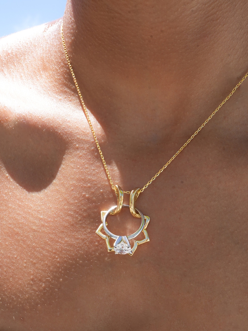 May include: A gold-toned necklace featuring a pendant shaped like a flower with a diamond ring at its center. The ring has a silver band and a clear, faceted stone. The necklace chain is also gold.
