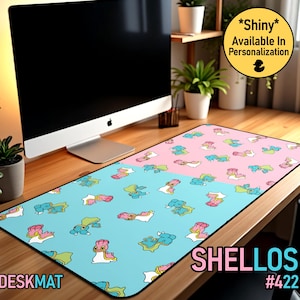 Puede incluir: Alfombrilla de escritorio rectangular con un diseño de dos tonos, con un fondo azul claro y rosa. La alfombrilla está cubierta con un patrón repetido de personajes de dibujos animados. La palabra "DESKMAT" está impresa en blanco en la parte inferior izquierda.