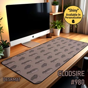 May include: A rectangular desk mat featuring a repeating pattern of cartoonish, grey and white creatures on a taupe background. The word "DESKMAT" is printed in white on the lower left corner. The text "CLODSIRE #980" is printed on the lower right corner.