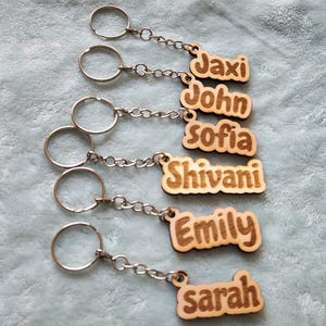 Peut inclure: Six porte-clés en bois avec des noms gravés dessus. Les noms sont Jaxi, John, Sofia, Shivani, Emily et Sarah. Chaque porte-clés a un anneau et une chaîne en métal argenté.