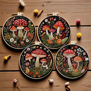 May include: Four embroidered mushroom art pieces in wooden hoops. Each features a red-capped mushroom with white spots, surrounded by colorful flowers and foliage on a black background. The hoops are displayed on a wooden surface.