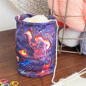 May include: A yarn bowl with a galaxy print design. The bowl is made of a soft, stretchy fabric and is perfect for holding yarn while knitting or crocheting.