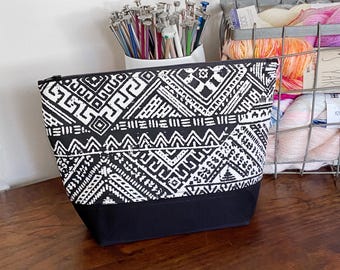 Pode incluir: Bolsa de zíper com padrão geométrico preto e branco com fundo preto. A bolsa está sobre uma superfície de madeira.