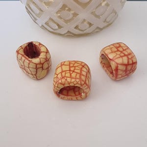 Peut inclure: Trois perles carrées en céramique avec un glaçage craquelé rouge et blanc. Les perles ont un trou au centre pour être enfilées.