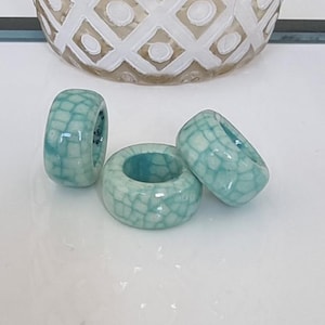 Peut inclure: Trois perles en céramique turquoise avec un glaçage craquelé blanc. Les perles sont rondes et ont un trou au centre.