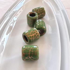 May include: Five green ceramic beads with a gold crackle glaze. The beads are round and have a hole in the centre.