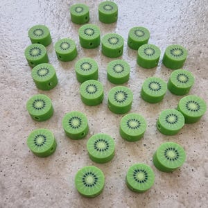 Könnte beinhalten: Eine Sammlung von 24 grünen und braunen Knöpfen in Kiwi-Form. Die Knöpfe sind in einem dreieckigen Muster auf einer hellgrauen Oberfläche angeordnet.