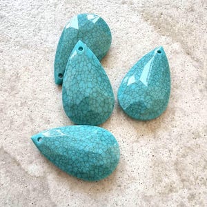 May include: Four turquoise teardrop-shaped glass beads with a crackled finish. The beads have a hole at the top for stringing.