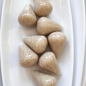 Op de afbeelding: Tien beige keramische kralen in druppelvorm met een gekrakelde glazuur.