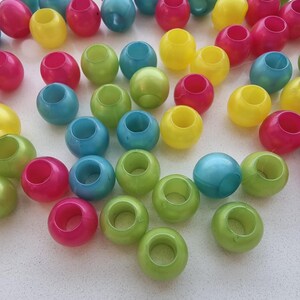 Può includere: Una collezione di perline di plastica colorate in varie tonalità di verde, blu, giallo e rosa. Le perline sono rotonde e hanno un foro al centro, il che suggerisce che siano per l'artigianato o per la creazione di gioielli.