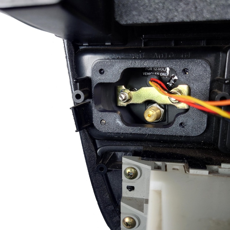 May include: Close-up of a black car stereo installation kit with a gold-colored metal bracket and a black plastic housing. The kit includes a connector with a gold-colored pin and wires with red, yellow, and black insulation. The label on the kit reads "FOR 12-VOLT VEHICLES ONLY".