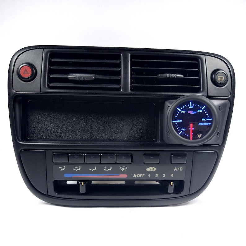 May include: Black dashboard with a boost gauge, climate control buttons, and a red hazard light button. The gauge has a blue face and a red needle.