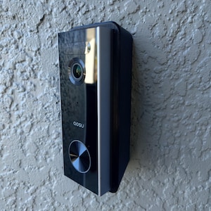 Może przedstawiać: Czarno-srebrny wideodomofon z okrągłym przyciskiem i nadrukiem "AOSU".