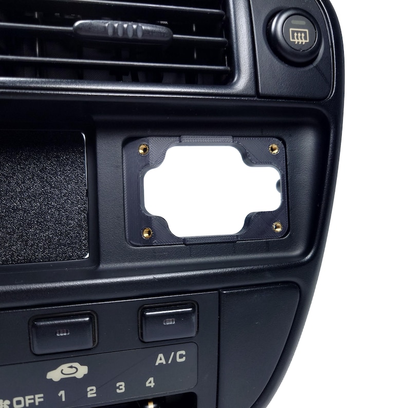 May include: Black plastic car dashboard with a blank rectangular cutout for a radio or other device. The dashboard has a few buttons and a small air vent.