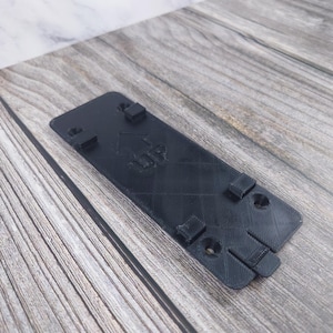 May include: Black plastic wall mount with four screw holes and the word "UP" printed on it.