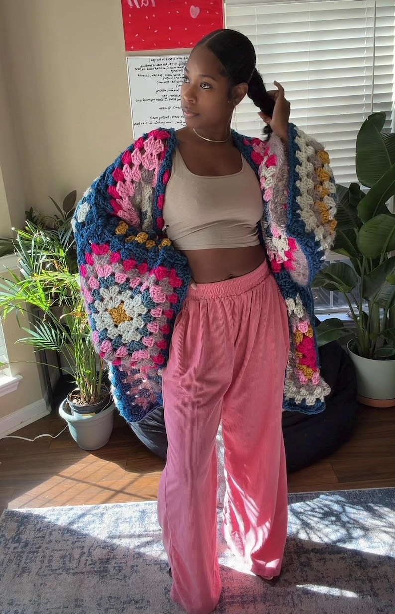 Peut inclure: Un cardigan crochet&eacute; &agrave; la main avec un motif de carr&eacute;s granny. Le cardigan pr&eacute;sente un m&eacute;lange de carr&eacute;s roses, bleus, jaunes et blancs. Port&eacute; avec un pantalon en velours c&ocirc;tel&eacute; rose et un haut court beige.