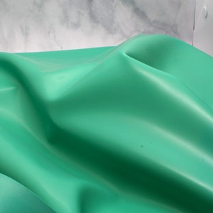 May include: Close-up of a teal fabric with gentle folds and curves. The material has a subtle sheen, with light creating highlights and shadows. The fabric's texture and form are emphasized by the lighting, creating a visually appealing image.