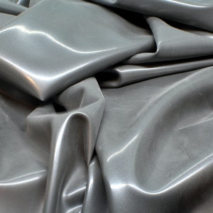 May include: A close-up of a smooth, gray fabric with a shiny, almost metallic finish. The fabric is folded and draped, creating soft, flowing lines.