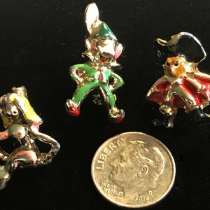 May include: Three small enamel pins featuring a mermaid, a jester, and a pirate. The pins are gold-toned and have colorful enamel details. The pins are about the size of a dime.