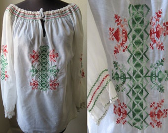 May include: White cotton blouse with long sleeves and a gathered neckline. The blouse features red and green embroidered floral designs.