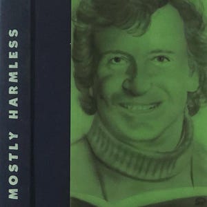 May include: A book cover with a green background featuring a portrait of a man with brown hair and a green sweater. The book title is "MOSTLY HARMLESS" and the author is "ADAMS".