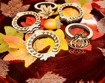 May include: A collection of wooden fall-themed coasters and decorative elements. The coasters feature intricate designs, including leaf and pumpkin shapes. The arrangement includes colorful autumn leaves and an acorn, creating a seasonal display.