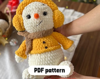 Peut inclure: Un bonhomme de neige crocheté avec un chapeau jaune, une veste et une écharpe marron. Le bonhomme de neige a un nez en carotte et des yeux noirs. Le texte "PDF pattern" est affiché.