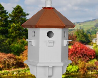 May include: A white birdhouse with a copper roof and a finial. The birdhouse has three nesting compartments and is mounted on a wooden post.