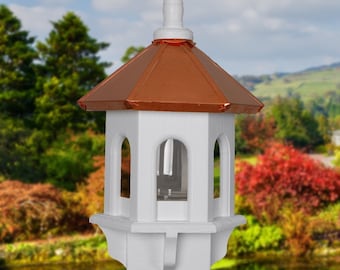 May include: White bird feeder with a copper roof and four feeding ports. The feeder is mounted on a wooden pole.