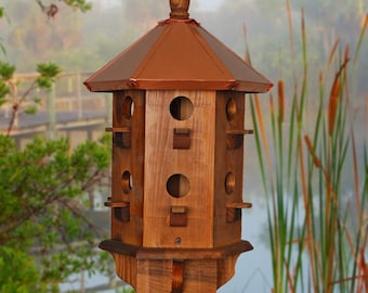 May include: A wooden birdhouse with a copper roof and multiple nesting compartments. The birdhouse is mounted on a wooden pole and has a hexagonal base.