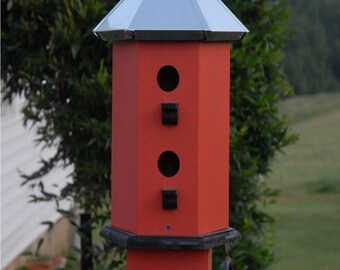 May include: A red birdhouse with a metal roof and three nesting holes. The birdhouse is mounted on a black metal post.