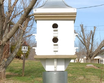 May include: A white birdhouse with a brown roof and a metal cylinder base. The birdhouse has multiple openings for birds to enter. The birdhouse is mounted on a wooden post.