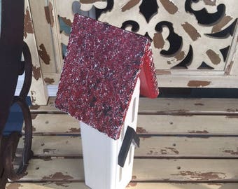May include: A small white birdhouse with a red roof. The roof is covered in a speckled red paint. The birdhouse has a small black door and a black window.
