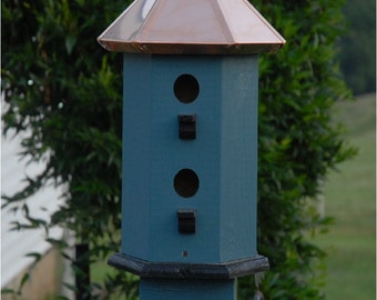 May include: A blue birdhouse with a copper roof and three nesting holes. The birdhouse is mounted on a wooden post.