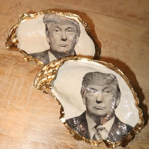 May include: Two oyster shells with gold trim, each featuring a black and white photo of the same person. The person is wearing a suit and tie.