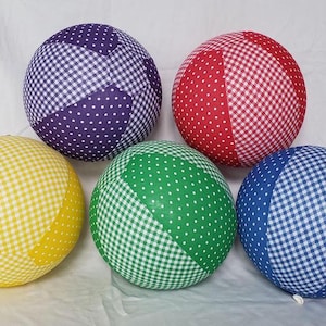 May include: Five fabric covered balls in different colors and patterns. The balls are purple with white polka dots and white gingham, red with white polka dots and white gingham, yellow with white polka dots and white gingham, green with white polka dots and white gingham, and blue with white polka dots and white gingham.