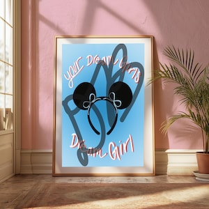 Pode incluir: Um pôster azul e branco com o texto "Your Dream Girl is Dream Girl" e uma faixa de orelha de Mickey Mouse preta com um laço branco.