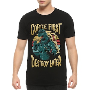 May include: Black t-shirt with a retro-style graphic of a Godzilla-like monster holding a cup of coffee. The text "Coffee First Destroy Later" is printed in gold on the shirt.