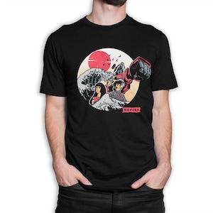 May include: Black t-shirt with a graphic print of a red robot, two people, and a wave. The graphic is set against a red sun and a blue sky. The text "超ダイモス" is printed on the bottom of the graphic.