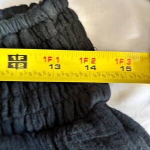 May include: Close-up of dark gray fabric with a textured appearance. A yellow tape measure shows a length of approximately 12 to 15 inches.
