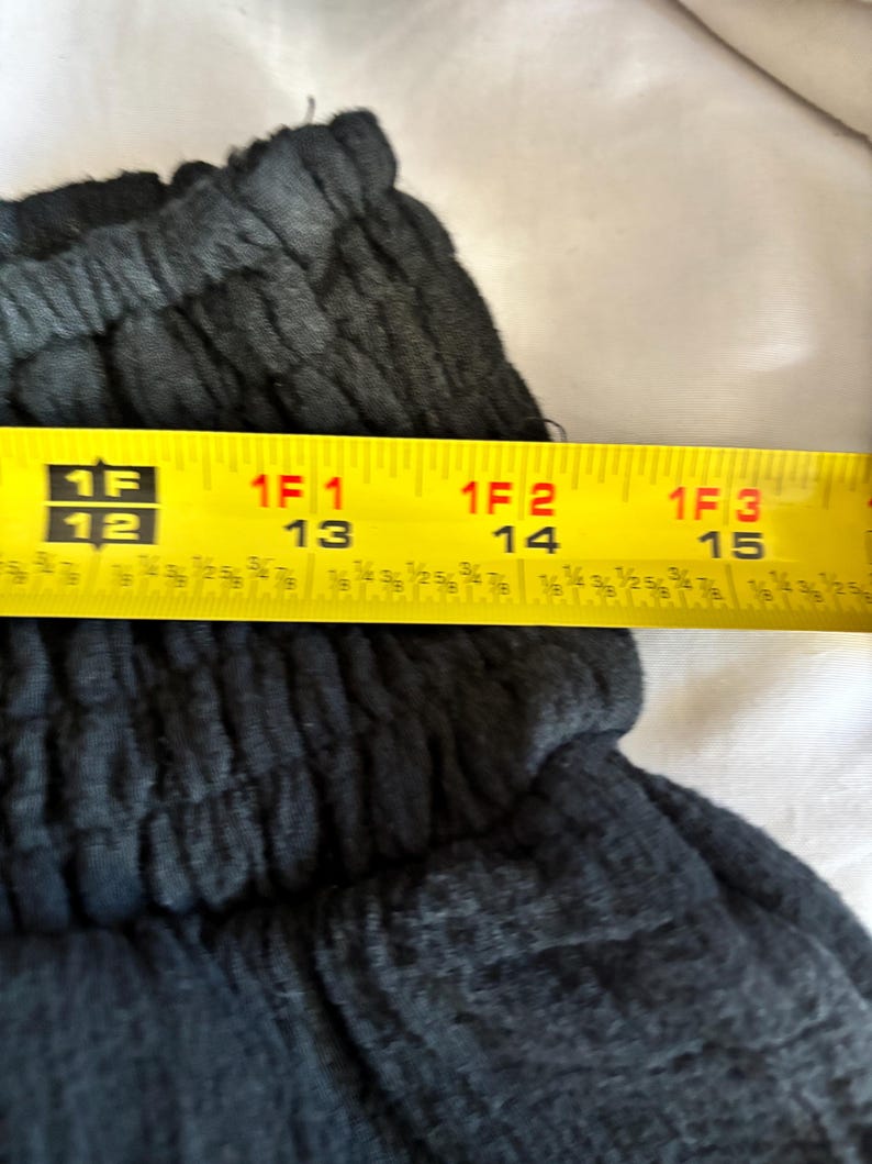 May include: Close-up of dark gray fabric with a textured appearance. A yellow tape measure shows a length of approximately 12 to 15 inches.