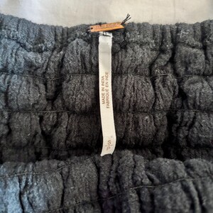 May include: Close-up of a dark gray garment with a textured, ruched design. A white tag with the text "MADE IN INDIA FABRIQU&Eacute; EN INDE" is attached. The tag also has the size "S/P".