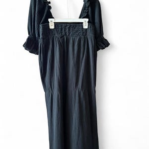 May include: A black two-piece outfit, consisting of a top and a skirt, hanging on a hanger. The top has short, ruffled sleeves and a square neckline. The skirt is long and flowing, with a gathered waistband. The fabric appears to be textured.