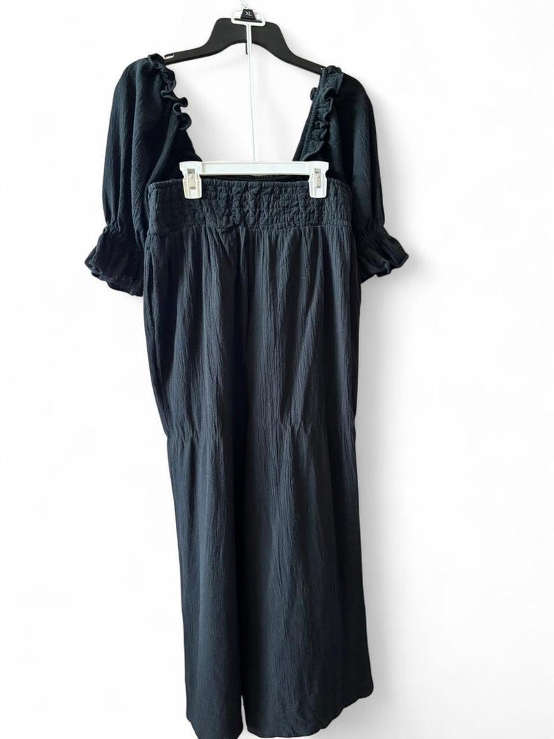 May include: A black two-piece outfit, consisting of a top and a skirt, hanging on a hanger. The top has short, ruffled sleeves and a square neckline. The skirt is long and flowing, with a gathered waistband. The fabric appears to be textured.