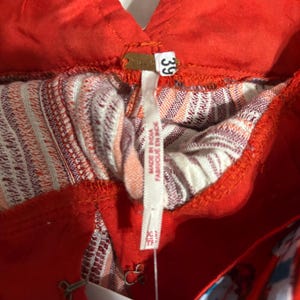 May include: Close-up of a red garment with a V-neck design. The garment has a patterned interior with shades of white, orange, and purple. A tag reads "Free People" and "39". The garment is labeled "Made in India".
