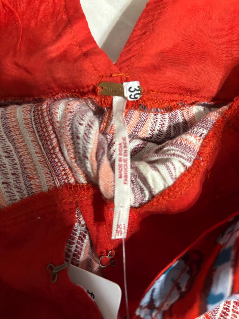 May include: Close-up of a red garment with a V-neck design. The garment has a patterned interior with shades of white, orange, and purple. A tag reads "Free People" and "39". The garment is labeled "Made in India".
