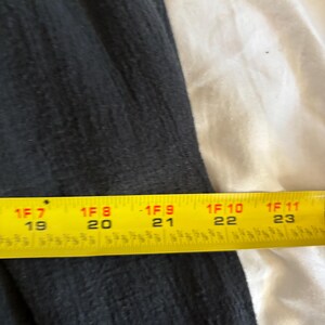 May include: A section of dark gray fabric with a textured surface. A yellow measuring tape is placed across the fabric, showing measurements from 19 to 23 inches.
