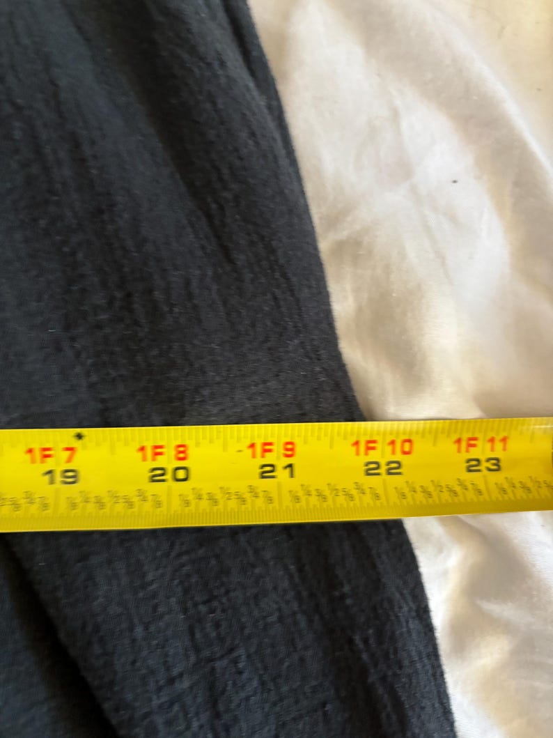 May include: A section of dark gray fabric with a textured surface. A yellow measuring tape is placed across the fabric, showing measurements from 19 to 23 inches.